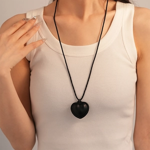 Close-up of a black heart pendant with woven texture detail on a long cord necklace