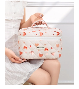 Close-up of quilted beige makeup bag with red hearts and BEENLOVE label being held