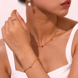 Detail of 18K gold-plated heart necklace and bracelet set on model with soft pink background