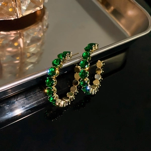 Macro detail of gold C-shaped hoop earrings with sparkling green zircon stones inlay