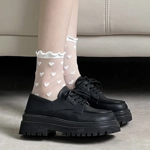 Détail de chaussettes blanches à motif cœur et mocassins noirs à semelle épaisse