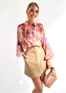 Détail d'une chemise à imprimé abstrait rose avec une jupe courte en cuir kaki à boutons