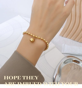 Detail of 18k gold geometric bead bracelet with round pendant on a model wrist