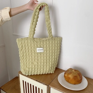 Dettaglio della borsa tote verde chiaro con texture a bolle e logo Love Sozakka su legno