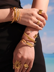 Close-up of a model wearing stacked gold bangles and rings with zircon on a beach