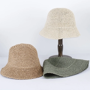 Three colors of foldable hand-woven straw bucket hats shown on wooden stand for summer