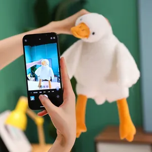Detail of plush white goose toy with orange beak and long legs held by hands