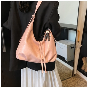 Detailed view of a pink crescent shoulder bag with a cute charm shown on a model