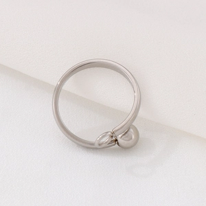 Minimalist silver stainless steel ring with ball accent and hanging loop on white fabric