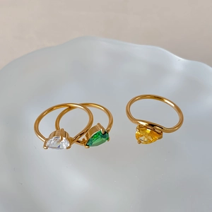 Detailed view of pear-cut water drop zircon rings in white, green, and yellow on a tray