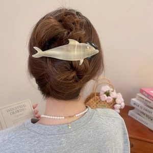 Detail view of a mother-of-pearl dolphin hair claw clip holding hair in a stylish bun