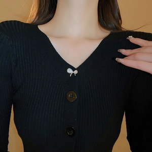 Détail d'une broche nœud en zircons brillants fixée sur un pull noir à col en V