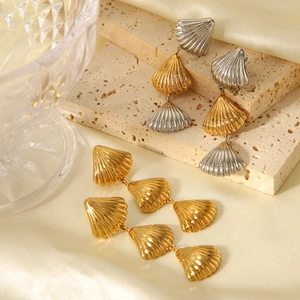 Macro shot of tiered shell-shaped gold and silver stainless steel earrings on silk cloth