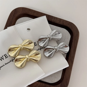 Set of four gold and silver metal bow hair clips displayed on a rustic wooden tray