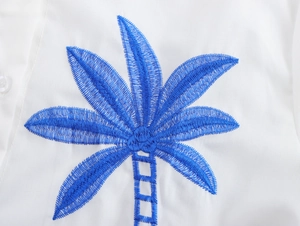 Close-up of blue coconut tree embroidery and button on a white resort wear top