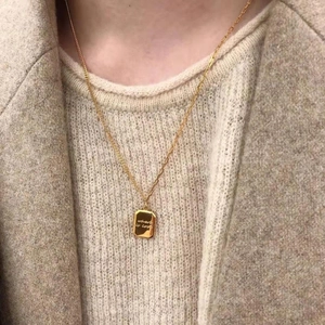 Detail shot of a rectangular gold pendant necklace with engraved Where is love text