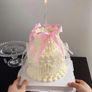 Elegant two-tier French cream cake with pink ribbon bows and silver wavy candle