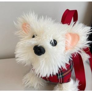 Detail of plush white dog doll wearing red plaid outfit with adjustable red shoulder strap