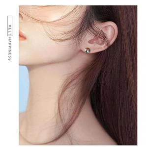 Close-up of a festive Christmas wreath earring worn by a model on a light blue background