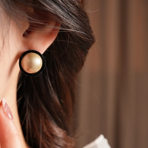 Close-up of vintage black flocked round earrings with gold center bead on a model