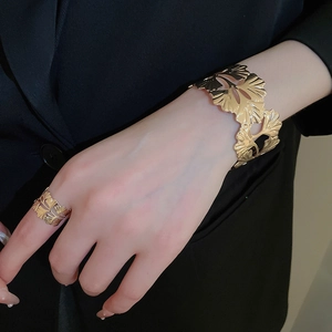 Detail of gold ginkgo leaf cuff bracelet and ring set worn on model over black blazer