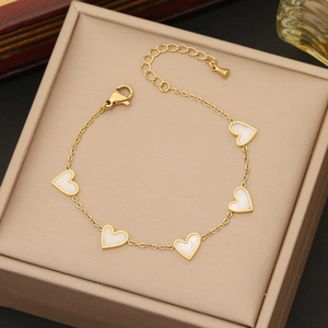 Elegant gold chain bracelet with five white shell heart charms in a beige jewelry box