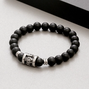 Detailed macro view of matte black beads with a silver skull charm on an elastic bracelet