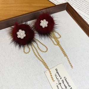 Detail view of burgundy faux fur pom-poms and pearl flower tassels on gold earrings