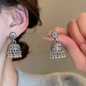 Close-up of vintage silver Jhumka earrings with intricate floral carvings and bell charms