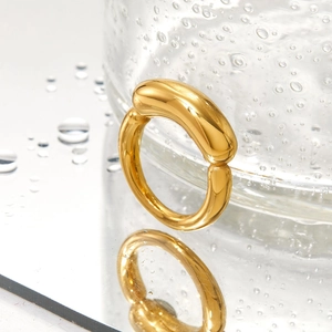 Minimalist gold stainless steel ring displayed on a water-beaded mirror surface