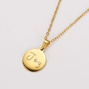 Macro shot of 18k gold plated round pendant with engraved Joy on stainless steel necklace