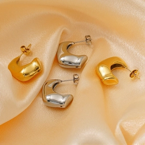 Close-up of chunky gold and silver C-shape earrings on pink silk background