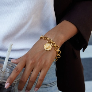 Detail of layered gold coin bracelet with angel relief on model's wrist with coffee cup