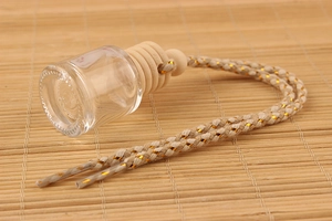 Detail shot of a transparent glass car perfume bottle with wooden lid on bamboo mat