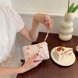 Floral makeup pouch with pink braided wristlet strap shown in a cafe setting