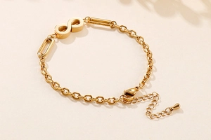 Detail of infinity symbol gold chain bracelet with lobster clasp on beige background