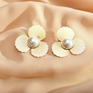 Elegant gold metal flower earrings with central pearl on champagne satin background