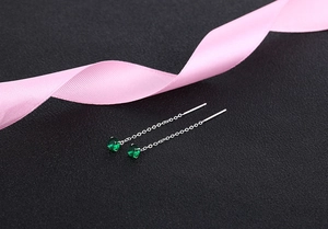 Detail of silver drop earrings featuring green zircon stones on pink silk ribbon