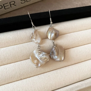 Vista macro dettagliata di orecchini di perle barocche con ganci metallici su vassoio beige