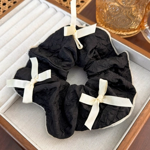 Detail of a black ruffled scrunchie with cream bows on a wooden tray with a vine background
