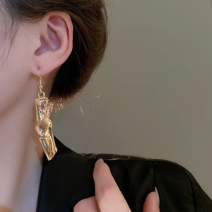 Close-up of gold irregular twisted geometric earrings worn by a model in soft lighting