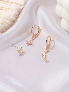 Detailed close-up of gold moon and star earring set with zircons on silk background