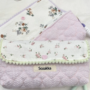Close-up of quilted floral pencil cases with heart buttons and pom-pom trim details