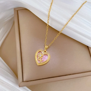 Close-up of a heart pendant with pink enamel and gold flower on a beige jewelry box