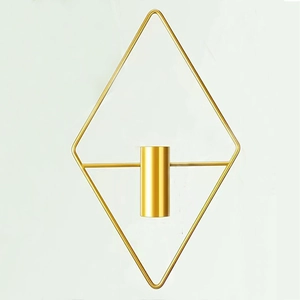 Detail of a geometric diamond shaped golden metal wall mounted candle holder on white wall