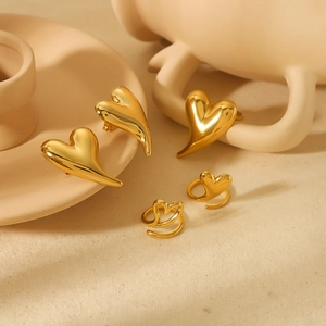 Polished 18k gold heart-shaped ring and earring set on a minimalist ceramic display