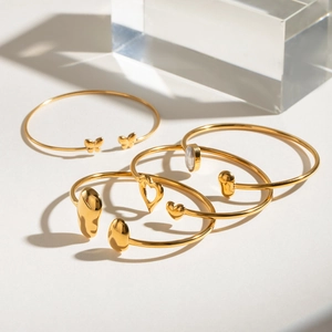 Set of 4 gold stainless steel open bangles with butterfly and heart charms on white background