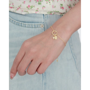 Detail of a gold bracelet featuring star and rectangle pendants on a model wrist