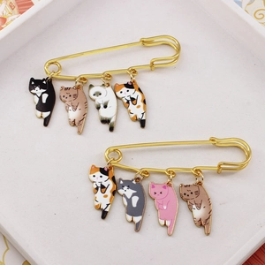 Macro detail of two golden safety pin brooches featuring cute hanging enamel cat pendants