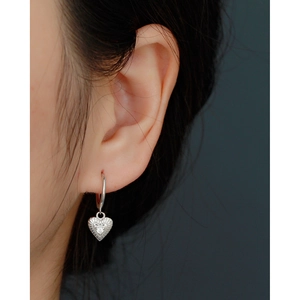 Detailed close-up of a silver heart drop earring with a centered zircon on a female ear